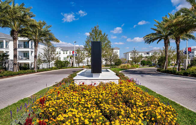 A black monument stands in a field of flowers with palm trees and buildings in the background.