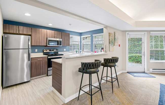 A kitchen with a refrigerator, stove, and bar stools.