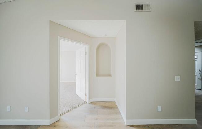 A white hallway with a doorway leading to another room.