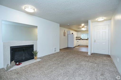 an empty living room with a fireplace and a kitchen