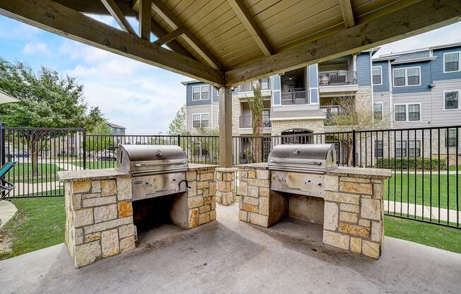 an outdoor kitchen with two bbq grills and a pergola