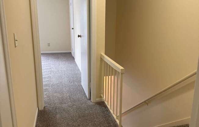A hallway with a carpeted floor and a staircase with white railings.