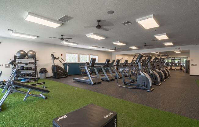 a large fitness room with cardio equipment and artificial grass