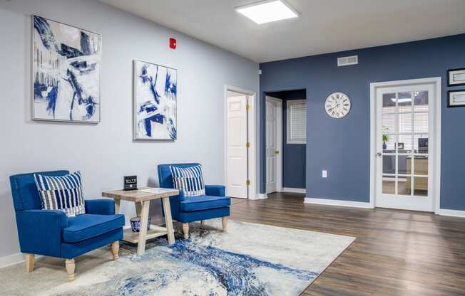 a living room with blue chairs and a table and a clock on the wall