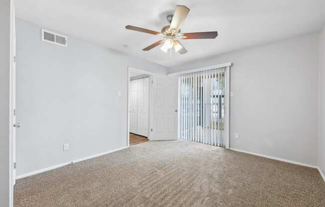 an empty living room with a ceiling fan and a door to a balcony