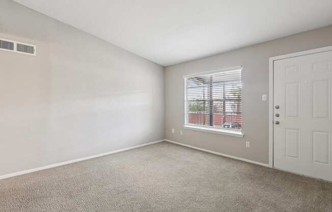 A room with a carpeted floor, a window with blinds, and a white door.