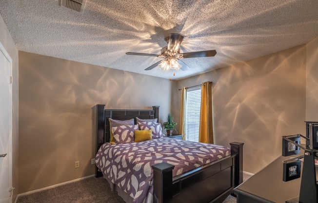 A bedroom with a bed, a ceiling fan, and a window with blinds.