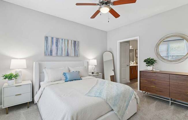 A bedroom with a large bed, a ceiling fan, and a mirror.