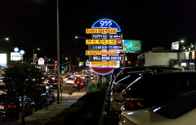 a busy street at night with cars parked on the side of the road