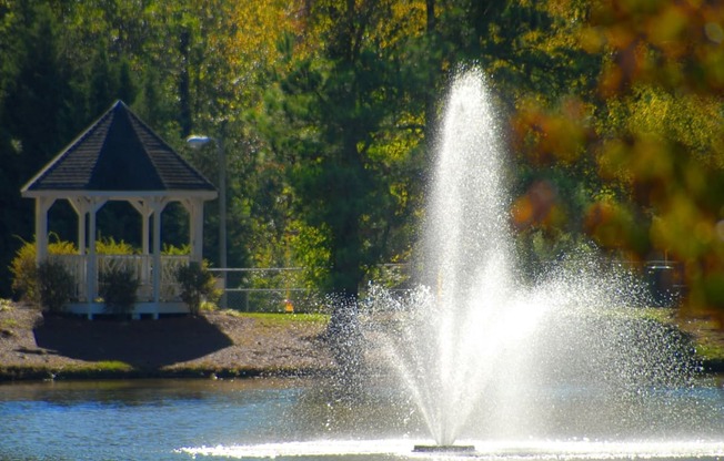 a fountain in a pond with a gazebo in the background