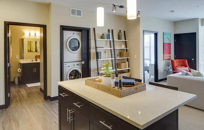Wide shot of apartment. Visible bathroom, washer and dryer, kitchen island, and living room couch
