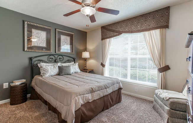 A bedroom with a bed, a ceiling fan, and a window with curtains.
