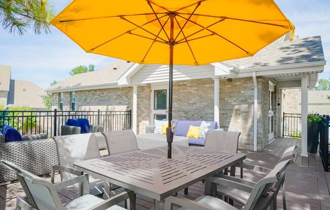 outdoor dining table and chairs shaded with a yellow umbrella on the sun deck of the community clubhouse