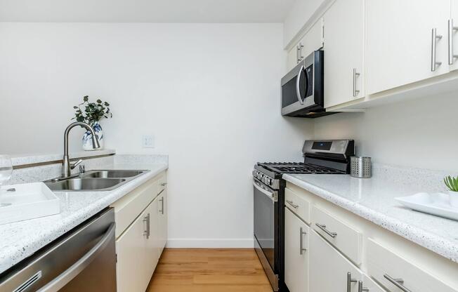 Modern kitchen featuring light-colored cabinetry, a stainless steel refrigerator, and an oven with a microwave above. The countertops are white with a subtle pattern, and there is a sink with a sleek faucet. A small plant and decorative items add a touch of style to the space.