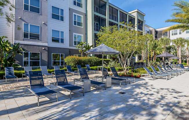 an outdoor lounge area with chairs and umbrellas in front of an apartment building