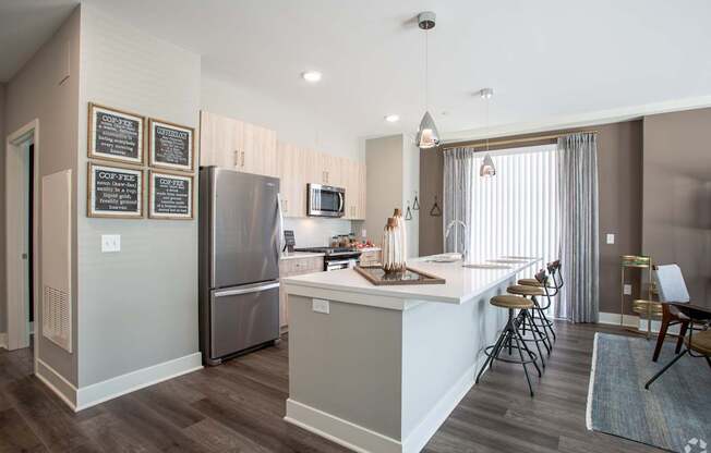 A kitchen with a refrigerator, bar stools, and a dining area.