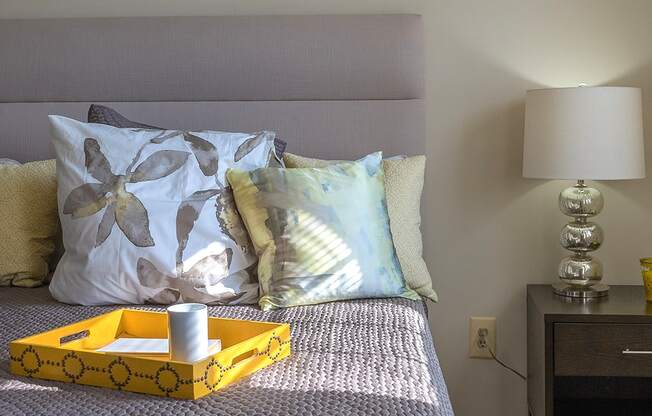 A bed with a yellow tray on it and a lamp on the nightstand at Dutch Village Apartments, Baltimore, MD