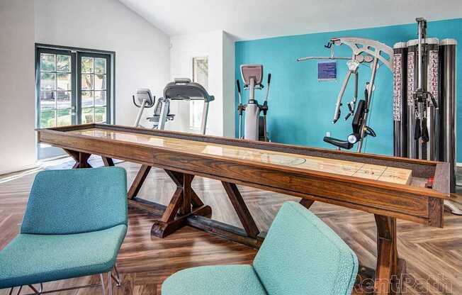A room with a wooden table, two chairs, and exercise equipment.