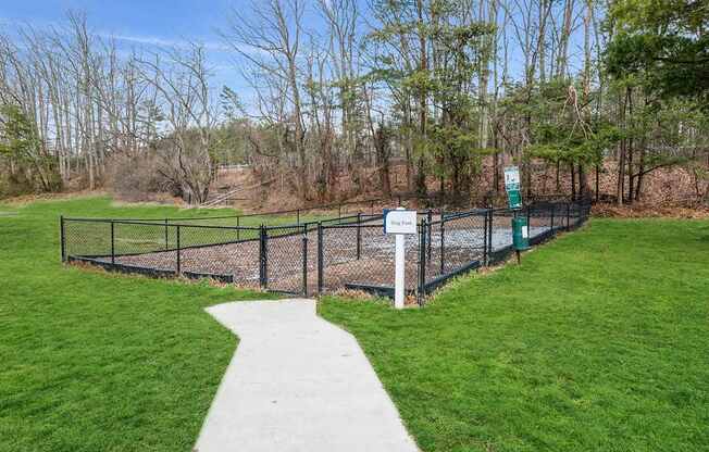 A sign in a park with a fence and a path.