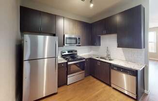 A modern kitchen here at BRIO at Firewheel with dark wood cabinets, granite countertops, white tile backsplash, stainless steel appliances, and wood-style flooring in a clean, updated layout.