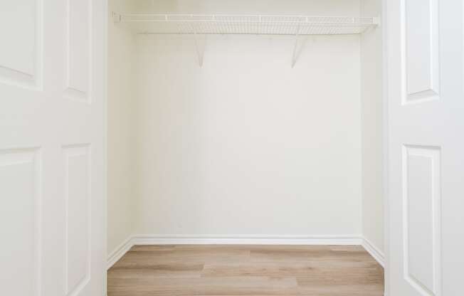 a walk in closet with white walls and wood floors
