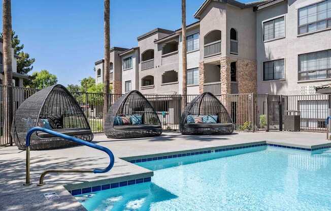 A swimming pool with a slide and two hanging chairs in front of apartment buildings. at Lazo Apartment Homes, Chandler, AZ 85225