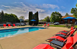 A pool surrounded by red chairs and a blue umbrella.