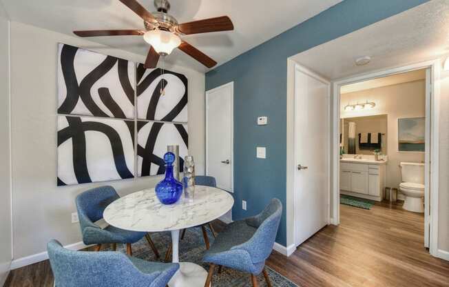 Dining Area with storage closet, Blue Chairs, Small, Round White Table, Ceiling Fan/Light and Abstract Painting on Wall