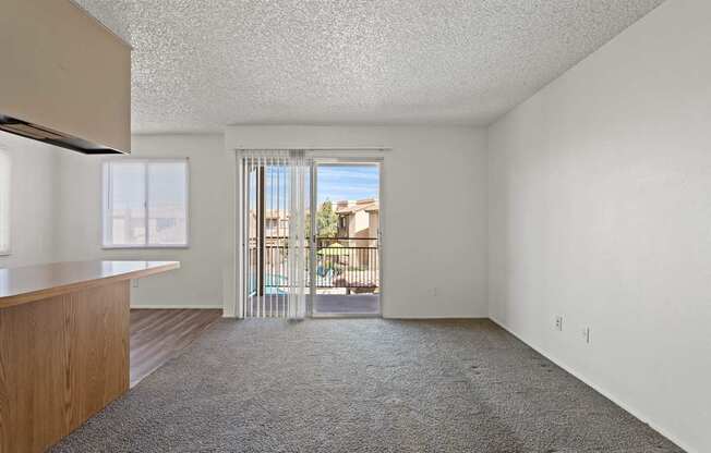 A room with a carpeted floor and a sliding glass door leading to a balcony.