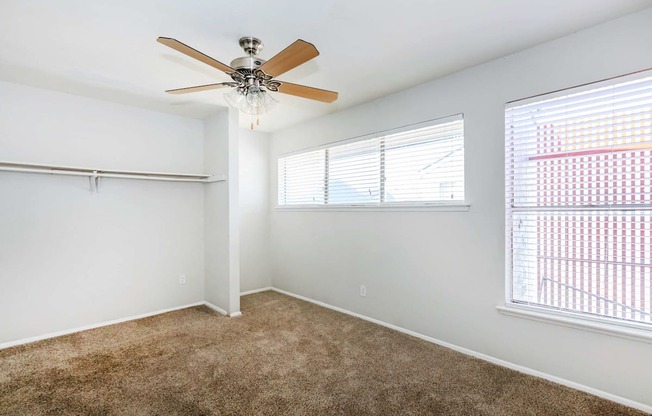 a bedroom with a ceiling fan and two windows