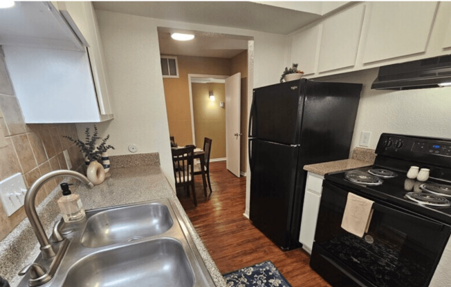 A kitchen with black appliances and a wooden floor.