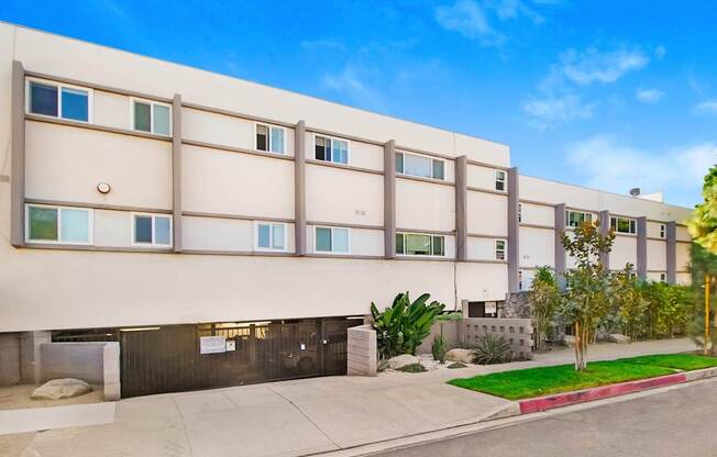 a white apartment building with a sidewalk and grass in front of it