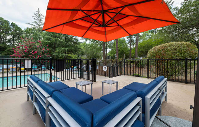 a poolside lounge area with blue couches and an orange umbrella