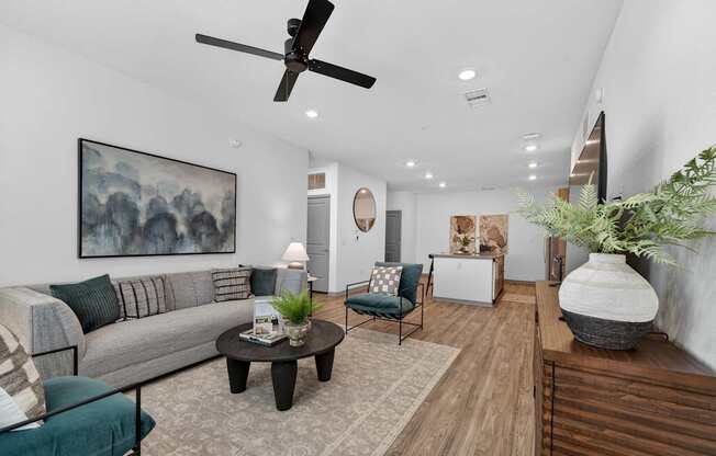 A living room with a grey couch, a coffee table, a ceiling fan, and a painting on the wall.