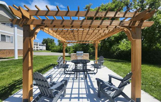 A wooden pavilion with a table and chairs and grill