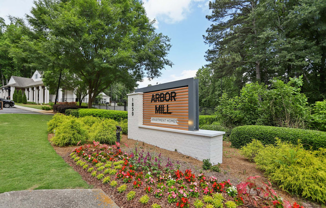 A sign for Arbor Mill is surrounded by flowers and greenery.