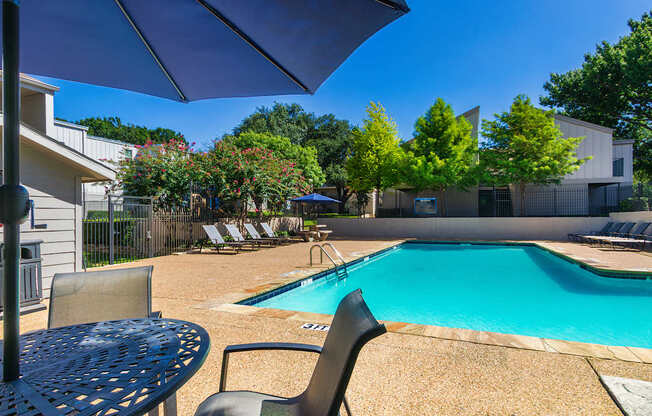 A pool surrounded by chairs and trees at The Biltmore Apartments located in the Vickery Midtown neighborhood of Dallas, TX.