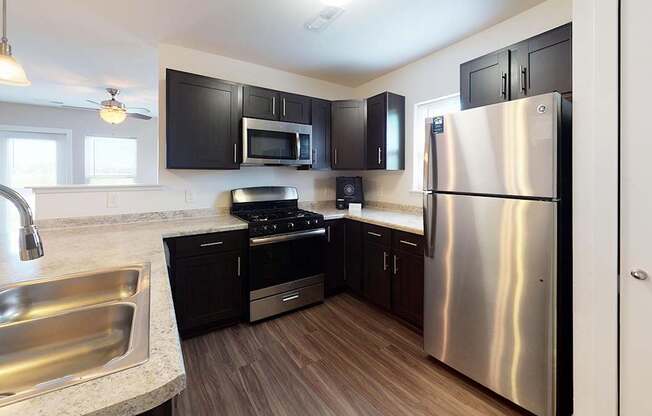 A modern kitchen with a stainless steel refrigerator, sink, and dark brown cabinets at Copper Creek Apartment Homes, Maize