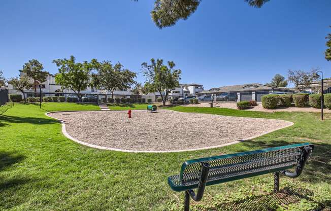 a park bench overlooking a gravel play area with a fire hydrant and trees