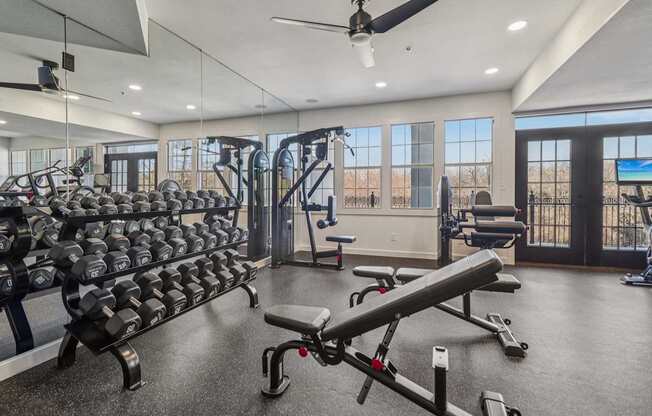 A spacious gym with a variety of equipment including dumbbells, weight machines, and a bench press.
