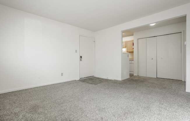 a living room with white walls and carpet and a door to a kitchen