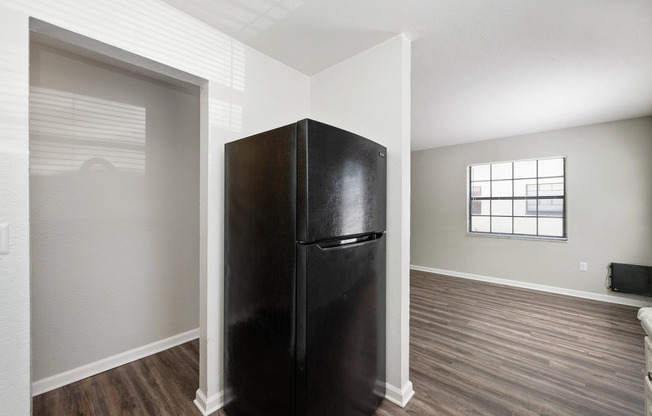 Modern apartment corner featuring a sleek black refrigerator, stylish hardwood flooring, and an inviting natural light-filled space with large windows.