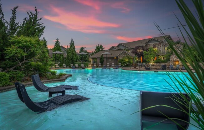 A pool with loungers and a house in the background during sunset.