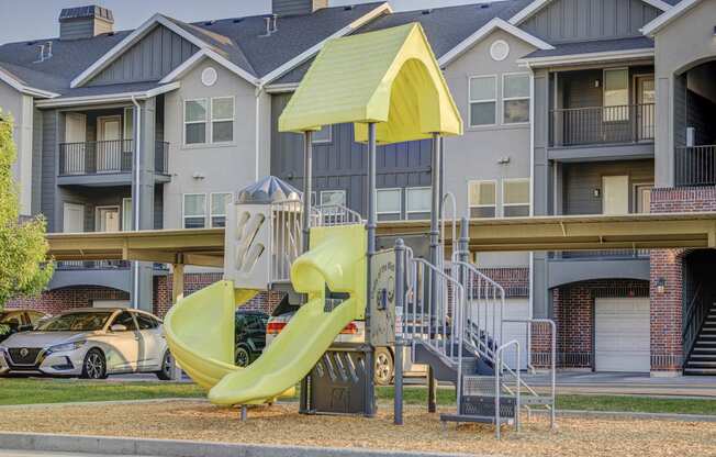 a playground with a yellow slide in front of an apartment building