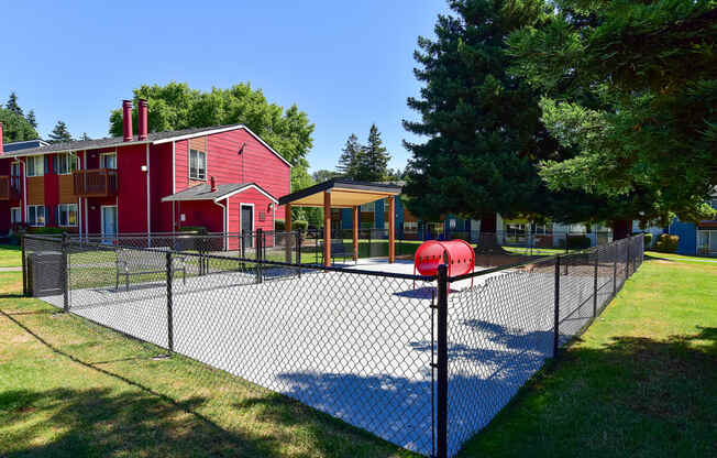 a fenced in tennis court with a red building in the background