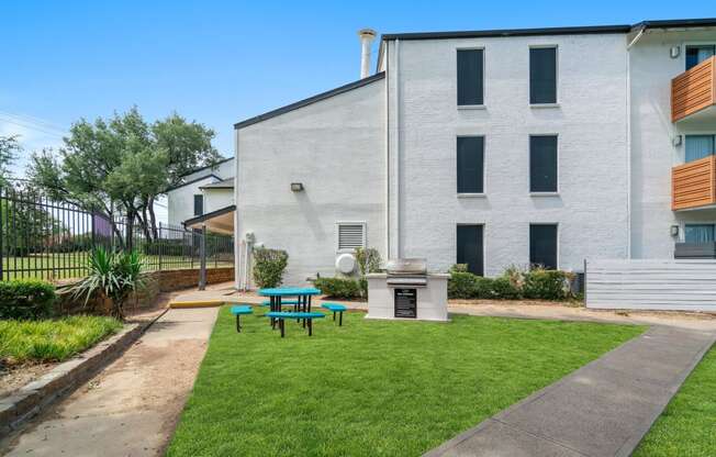 a patio with a grill and picnic table in front of a white building