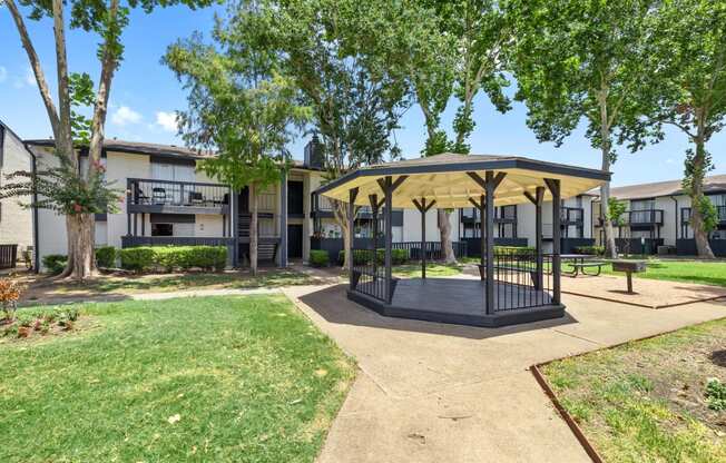 a gazebo with trees and apartments in the background