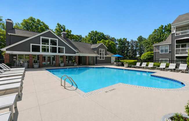 A large swimming pool in front of a house with a deck and lounge chairs.
