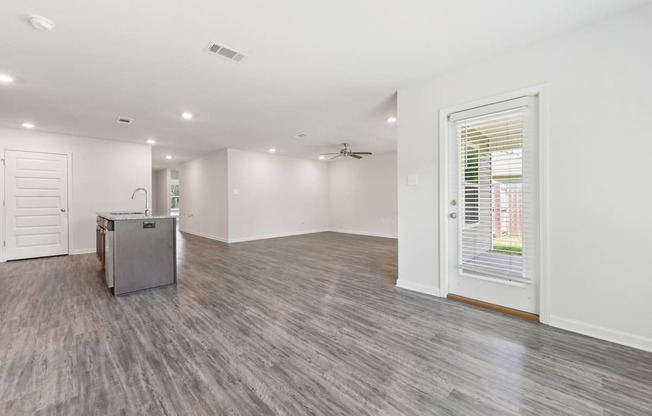 an empty living room with a kitchen and a large window