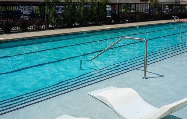 A swimming pool with white lounge chairs and apartment buildings in the background.